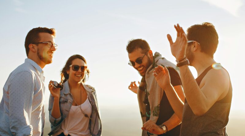 A group of friends laughing and dancing outdoors on a bright sunny day, showcasing friendship and joy.